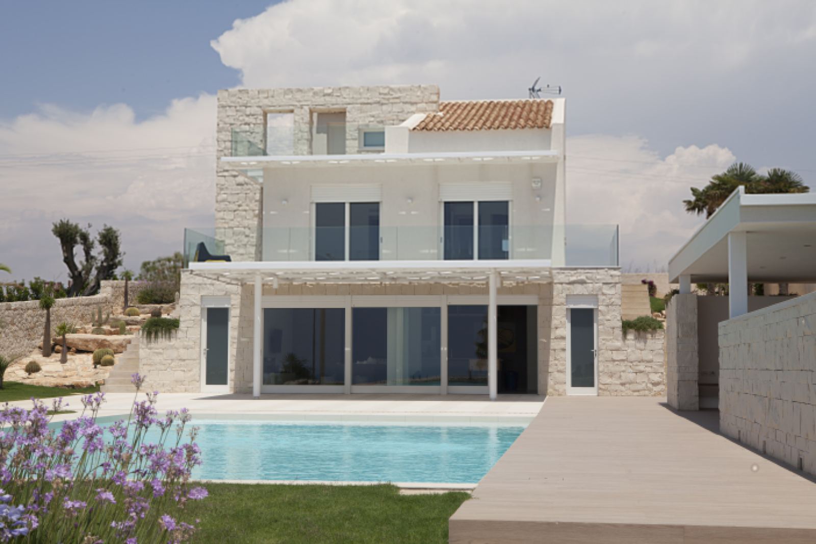 Piscina con deck in legno davanti a una villa in pietra