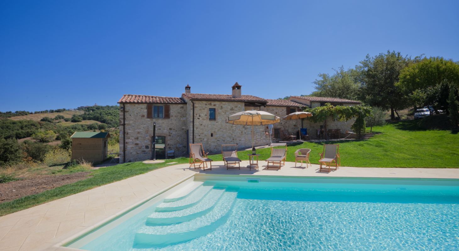 Piscina con scala romana e solarium davanti a un casale in pietra