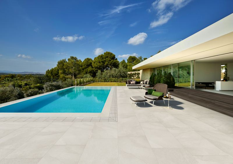 Piscina interrata con bordo in gres chiaro accanto a una villa moderna